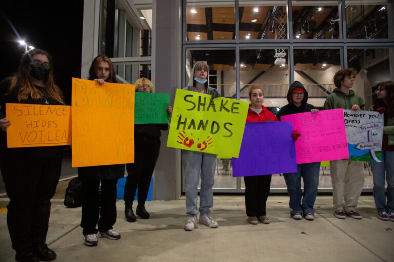 About two dozen students hold colorful signs in protest before a school board meeting at Options High School.