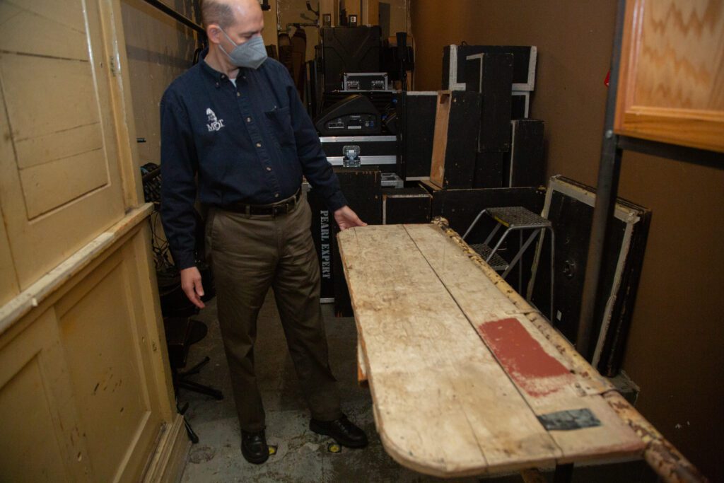 John Purdie holds an aged, wood table leaf up put inside the storage room at the backstage.