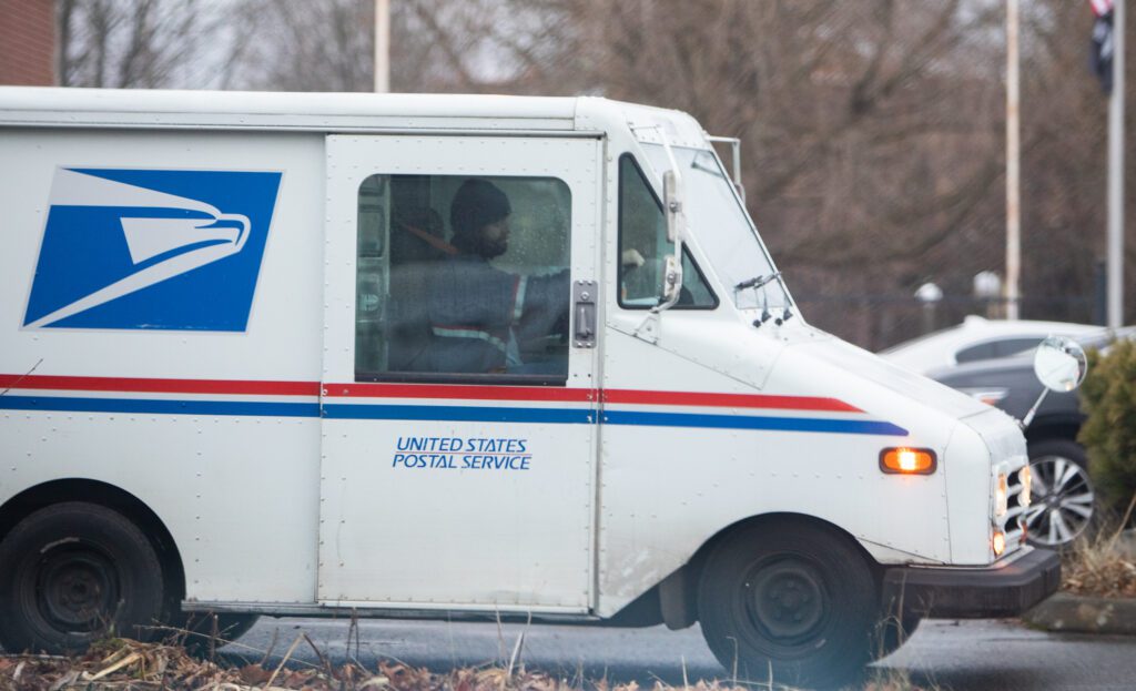 A postal worker departs the U.S. Post Office with rain droplets covering the windows of the van.