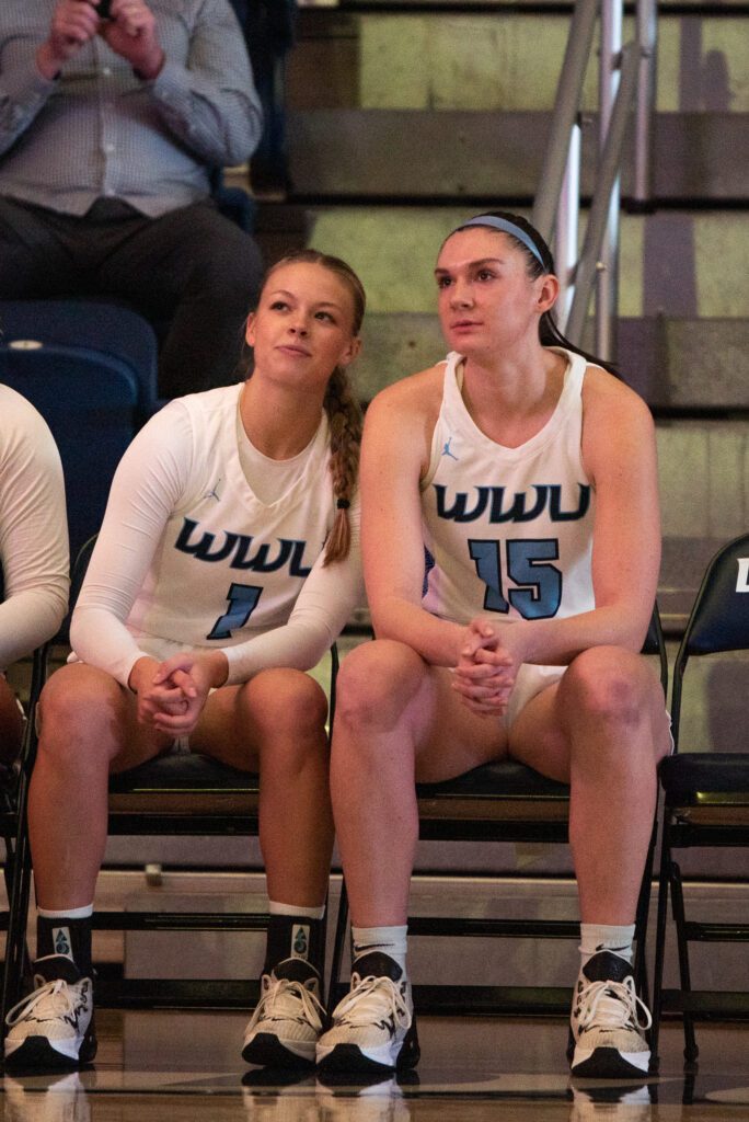 Walling (15) looks up at a pregame hype video with senior guard Avery Dykstra (1) while seated on the sidelines.