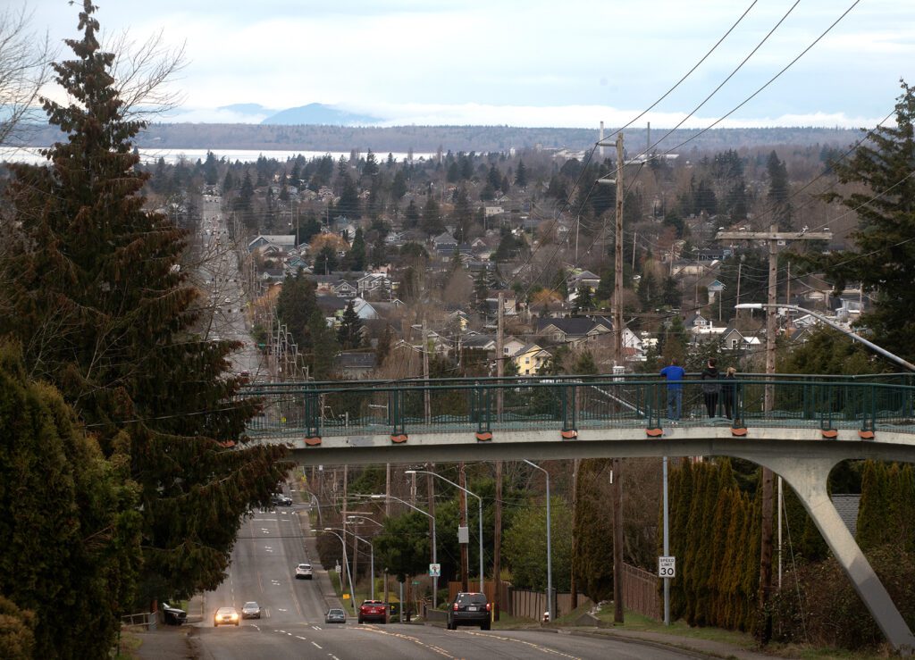 Three pedestrians look toward Bellingham Bay from the Railroad Trail above Alabama Street as cars drive past underneath the bridge.