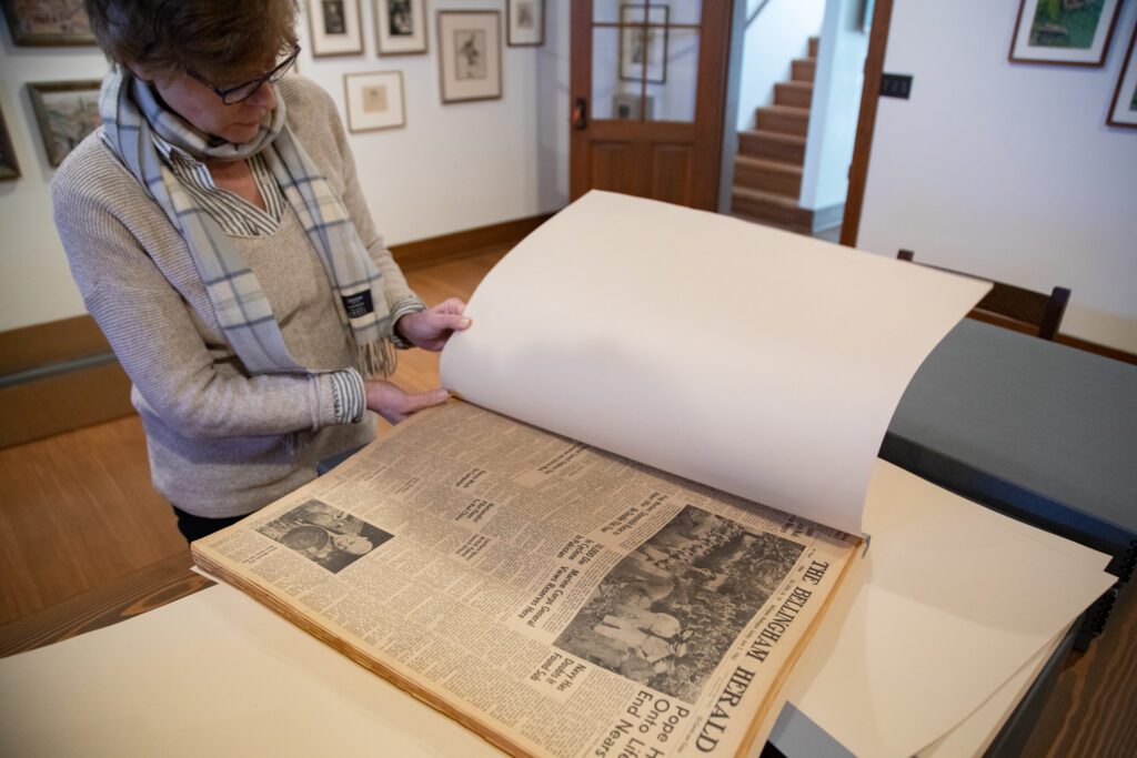 Tour guide Heidi Wassan opens a bound book of copies of The Bellingham Herald from 1963 on a large table.