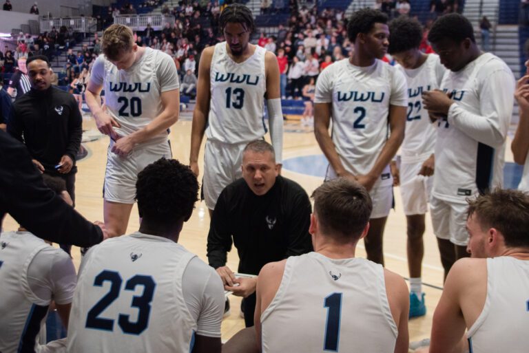 Head coach surrounded by his team wearing their signature white uniform strategize during a timeout.