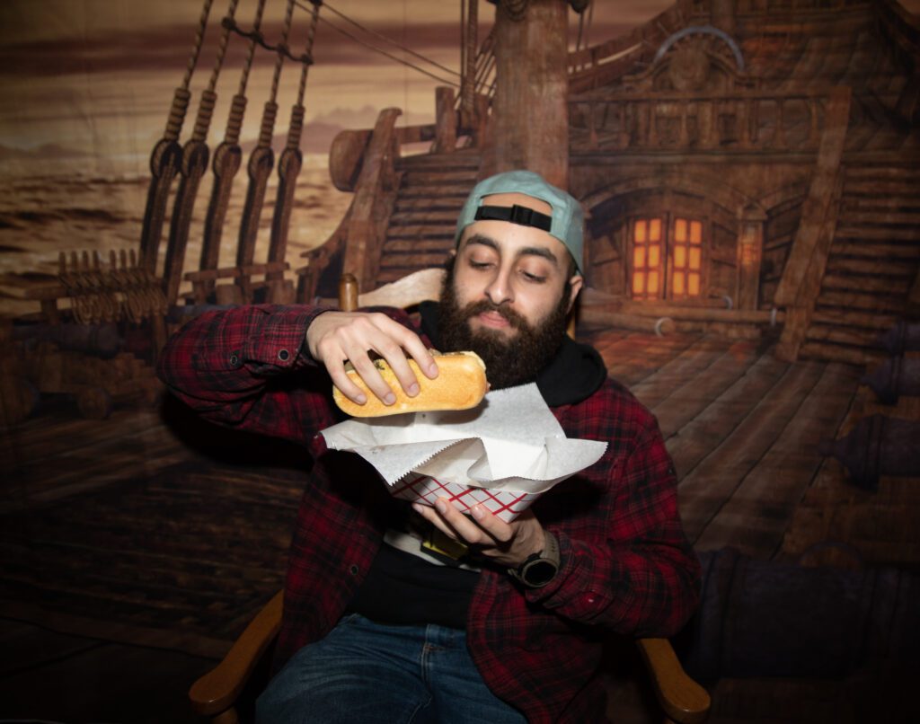 Mark Saleeb finishes the night with a hot dog from El Capitan's as he is seated in front of a pirate ship mural.