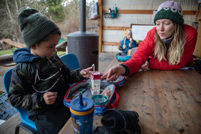 Leo, left, gets help with a tipping juice box from teacher Lizzy Chandler.