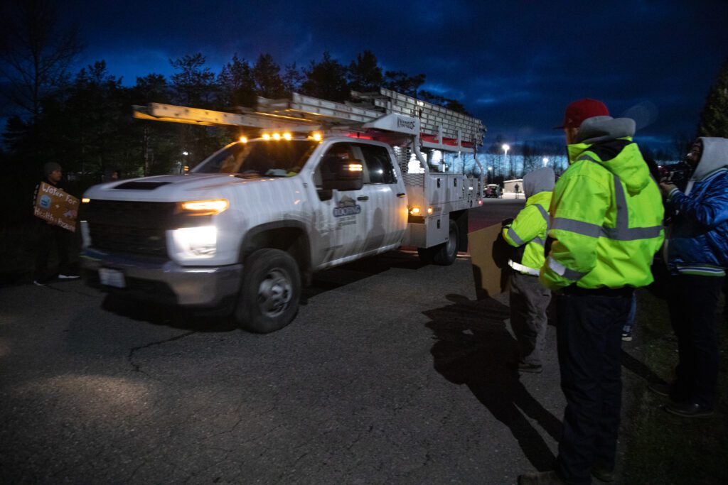 A Mt. Baker Roofing truck drives past the crowd of employees and protestors.