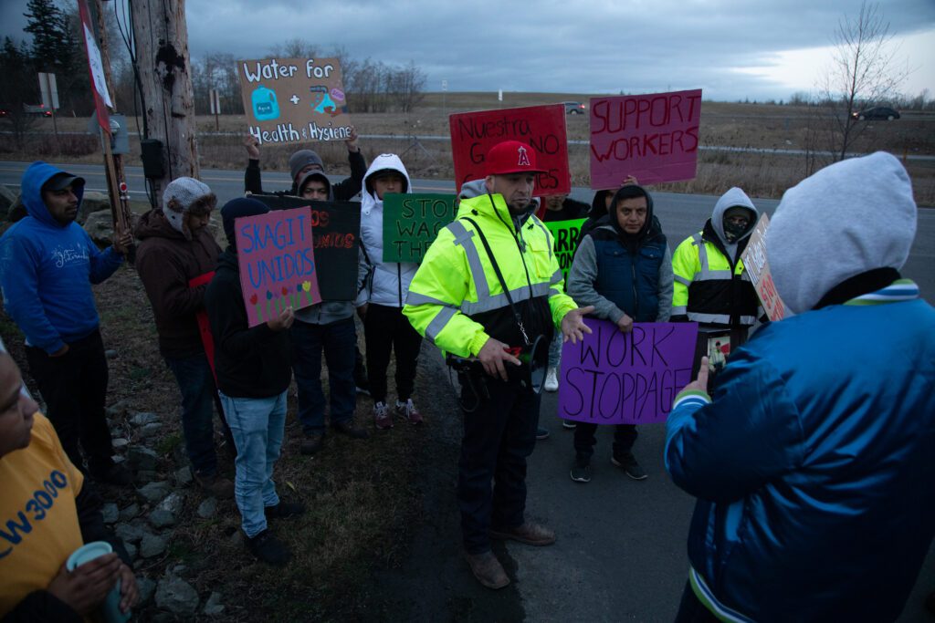 Familias Unidas Por La Justicia president Ramon Torres livestreams the picket with Mt. Baker Roofing workers holding protesting signs.