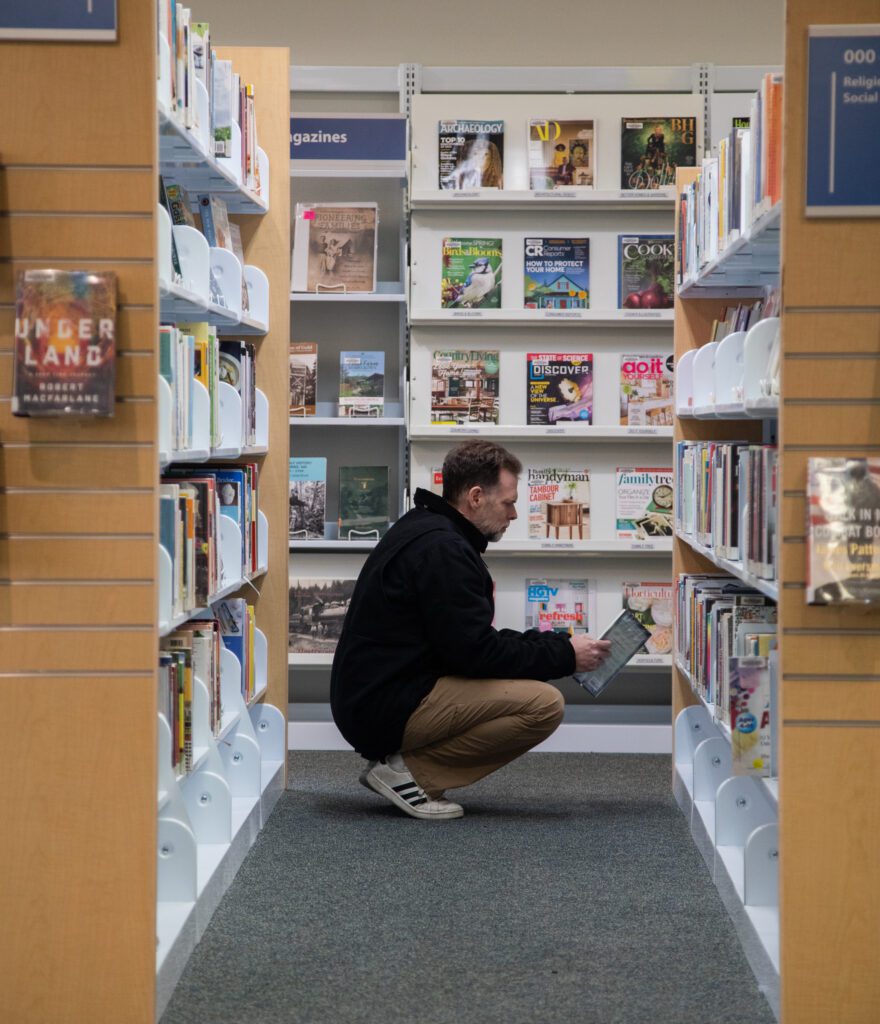 Brent Leggett squats to look at a book in the Sumas Library.