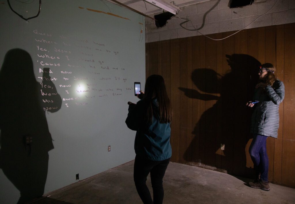 Emily Martens and Maggie Spinelli takes a photo of the prayer on the wall with her phone.