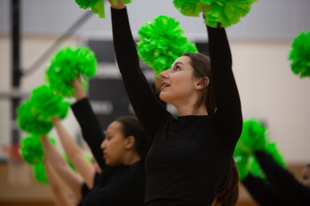 Frankie Capristo looks up with her green pom poms next to her peers.