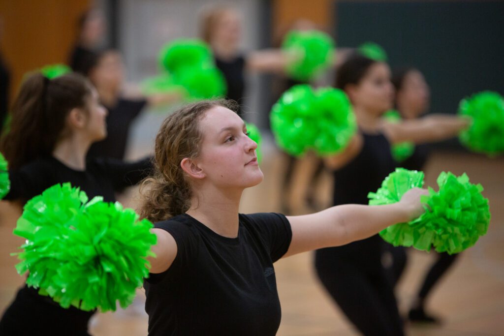 Arms wide, Sierra Hawes extends both her arms with the green pom poms alongside her peers.