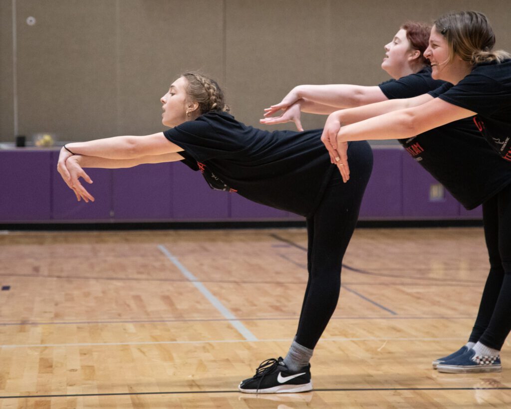 From left, Sage Cary, Ava Geracie and Isabelle Benjamin practice as they lean forwards with their hands together.