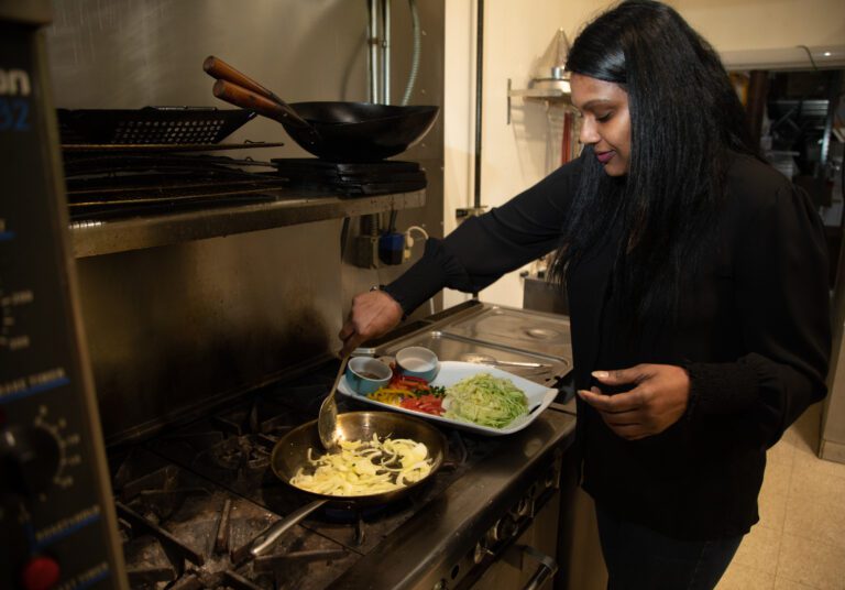 Sarah Chan cooks a cabbage stir fry with onions, bell peppers and spices on a stove top.