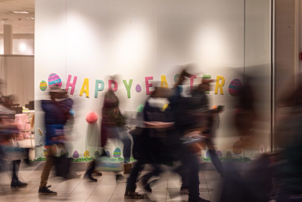 Parents and children rush to the starting point of the Easter egg hunt, past a wall decorated for easter.