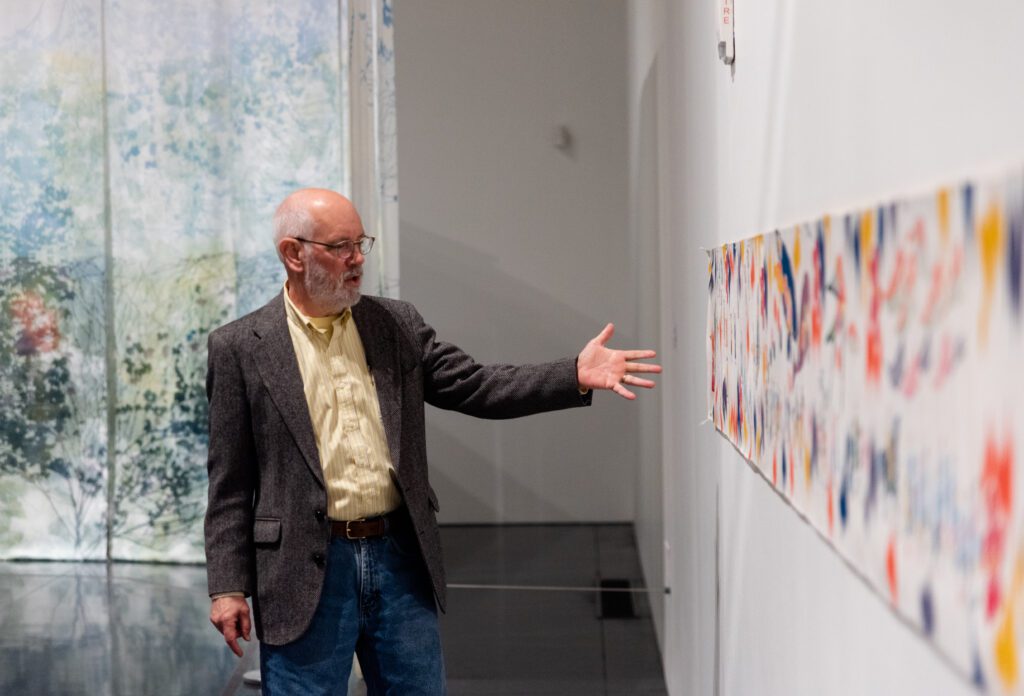 Brower shows off Yuken Teruya's linen work "Parade From Far Away, 2014," while talking to the attendees.