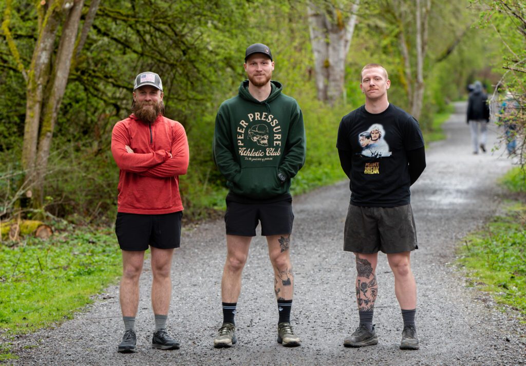 The three men behind the Dawson Construction team pose for a photo on a trail.