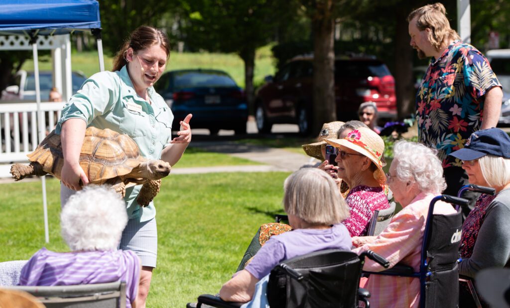 April Jackson shows a tortoise named SpongeBob ScalePants to residents, with some taking pictures with their phone.