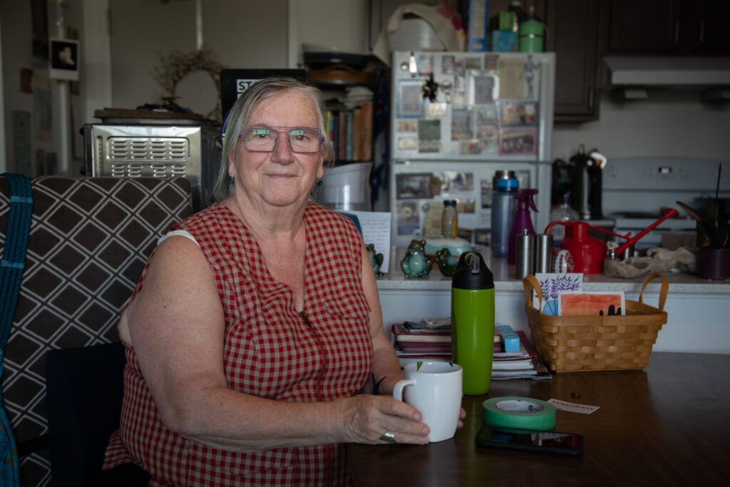 Catherine Chambers sits at her dining room table in her apartment with a mug in hand.