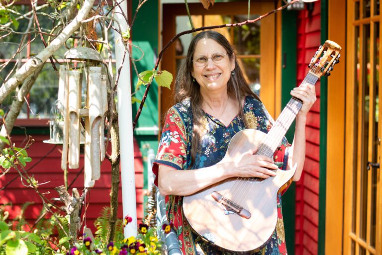 Fl!p Breskin holds her guitar in her colorful backyard next to her windchimes.