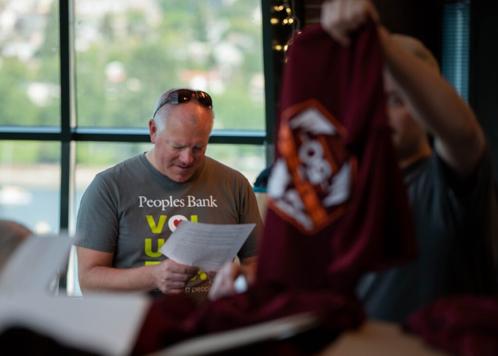 Paul Brock reads off T-shirt sizes to other volunteers who are holding up the clothes to eye-level.