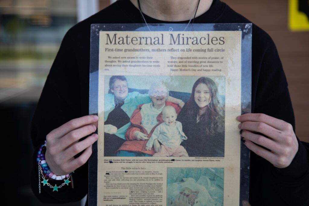 Adrian Cairns holds up a print of a 2005 Bellingham Herald article about Cairns at 11 months old with her family.