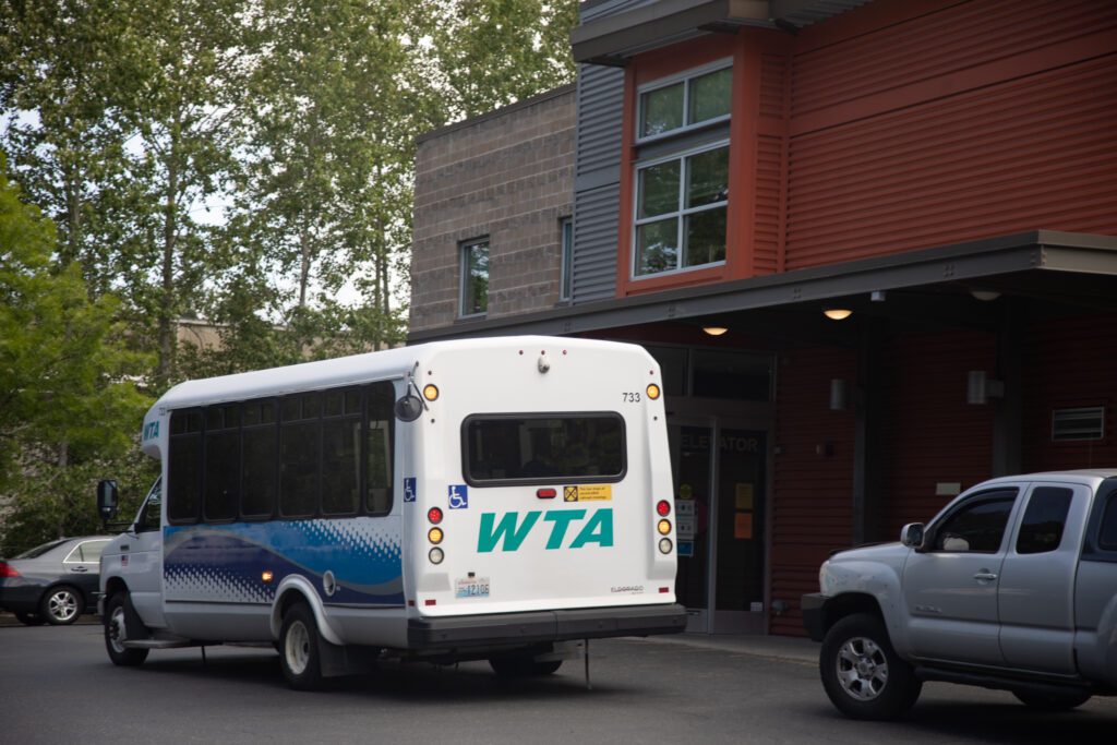 A WTA paratransit bus makes a stop off Birchwood Avenue near other parked cars.