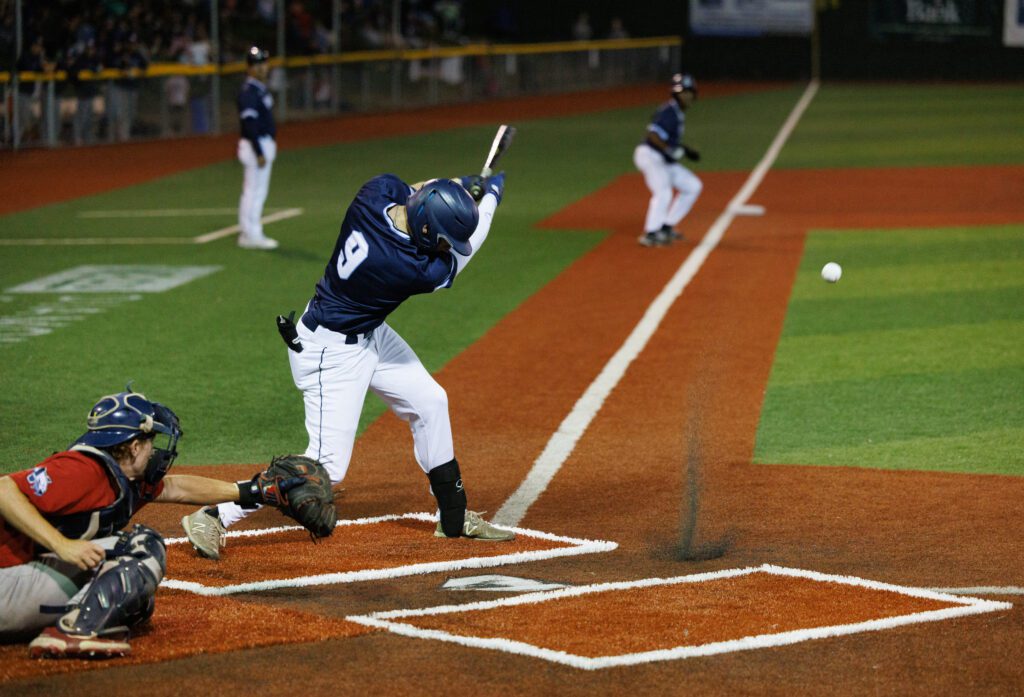 Noah Meffert hits a grounder as the ball bounces off the red ground.