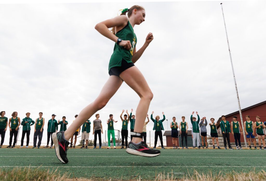 A young girl races past the boy's cross country team as they do the wave from the sidelines.