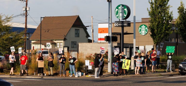 Unionized Starbucks workers and their supporters on strike outside the Iowa Street location with multiple signs.