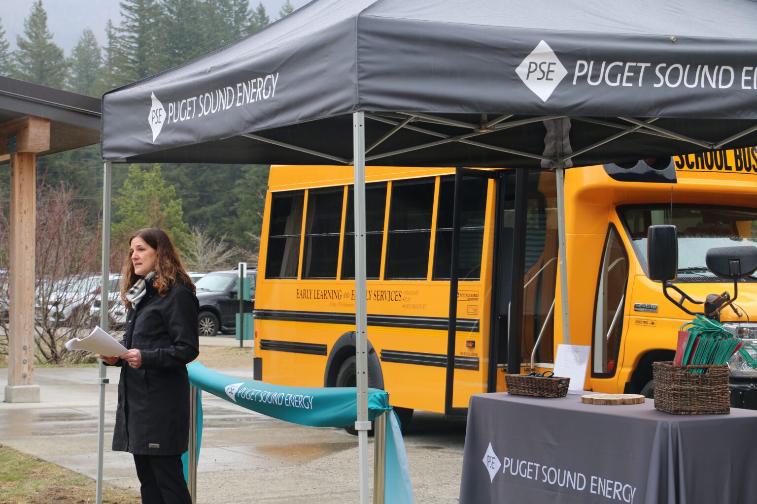 Heather Mulligan speaks next to a canopy near the yellow school bus.