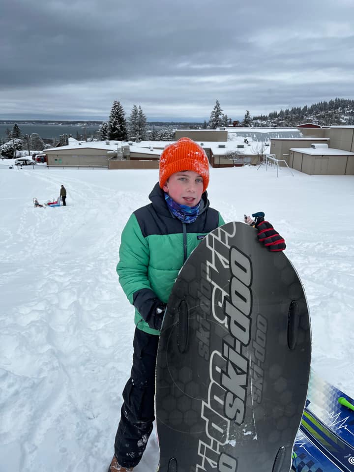 A child holds up his sled at the top of the snow hill.