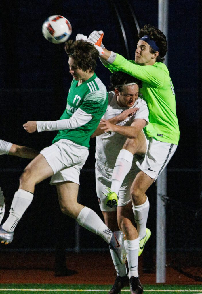 Bellingham goalie Henry White punches the ball away as he clashes with another player.