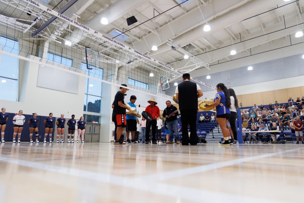 Lummi Nation and Ferndale High students perform a load recognition ceremony next to the volleyball net.