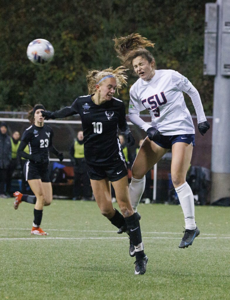 Western Washington University’s Claire Potter heads the ball away from a Columbus State defender as they both make expressions as they brace for impact.