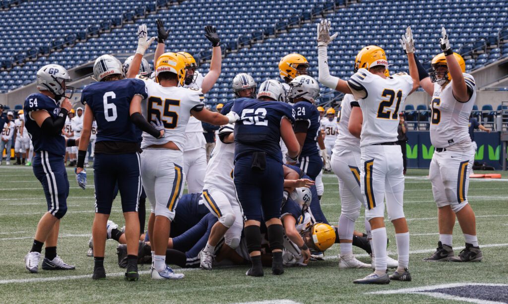 Teammates signal a touchdown by Isaiah Carlson as they surround the pile of players on the ground.