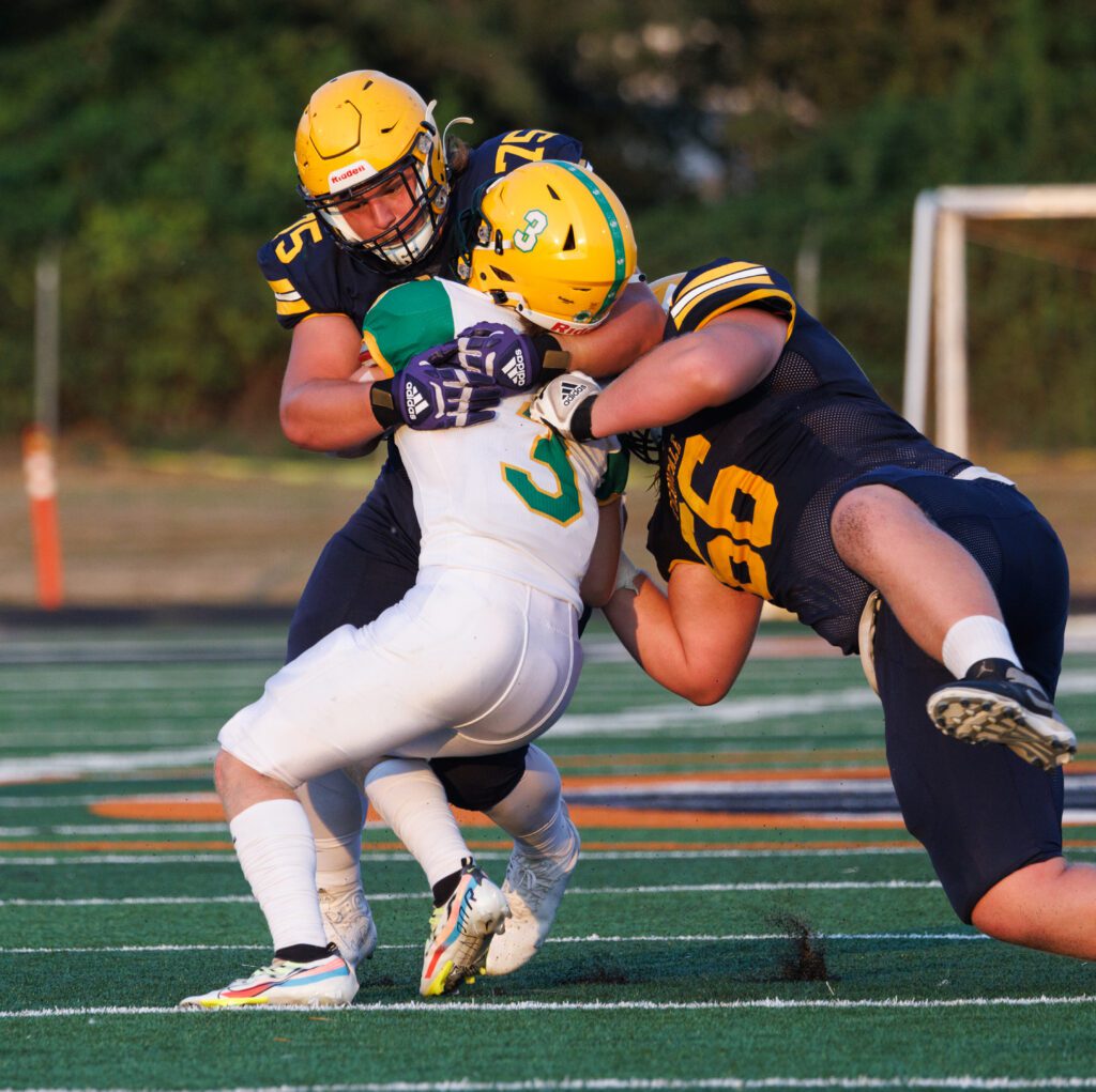 Kaedan Hermanutz tackled by Camden Raymond as Landen Hatchett dives as he's holding the back of his jersey.