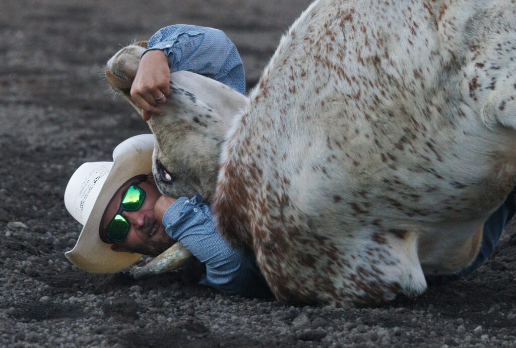 Ty Sherman straddles a bull down to the ground with sunglasses on.