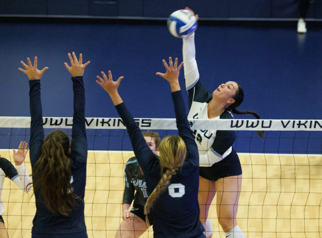 Gabby Gunterman spikes the ball over the net as two defenders raise their arms to block the shot.