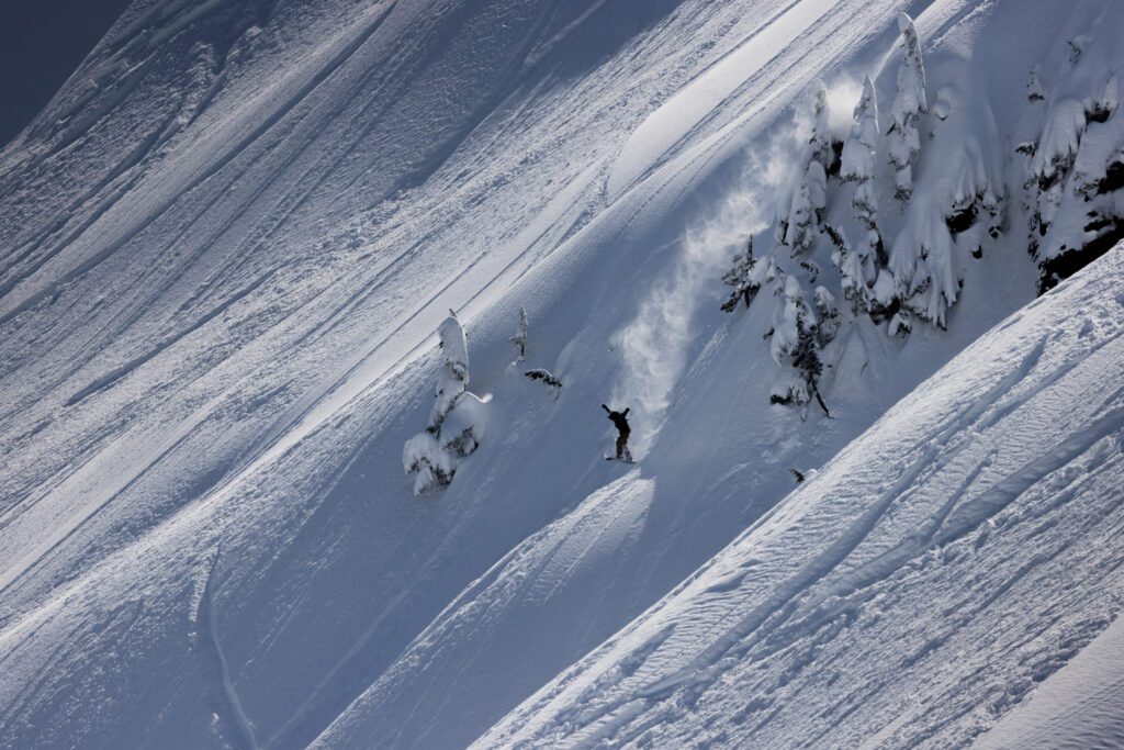 A snowboarder descends Mount Baker with a trail of snow dust behind them.