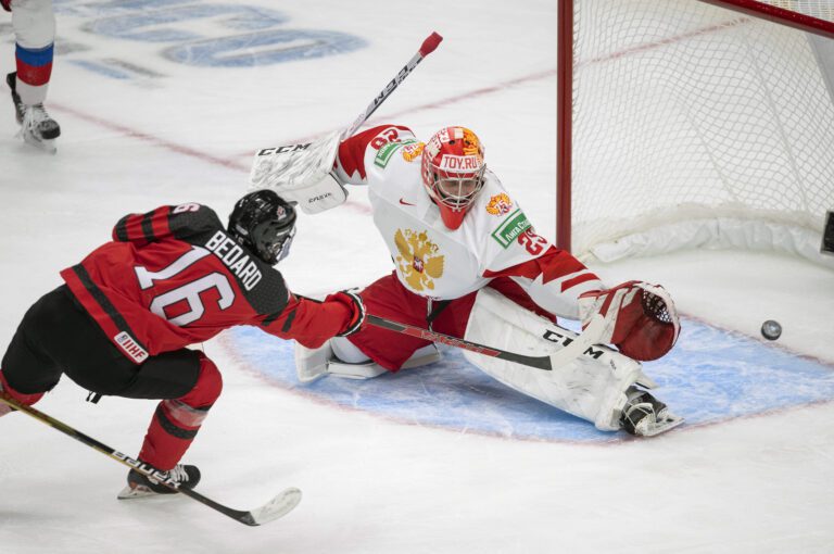 Canada's Connor Bedard (16) scores on Russia goalie Yegor Guskov (29) as they both dive for the puck.