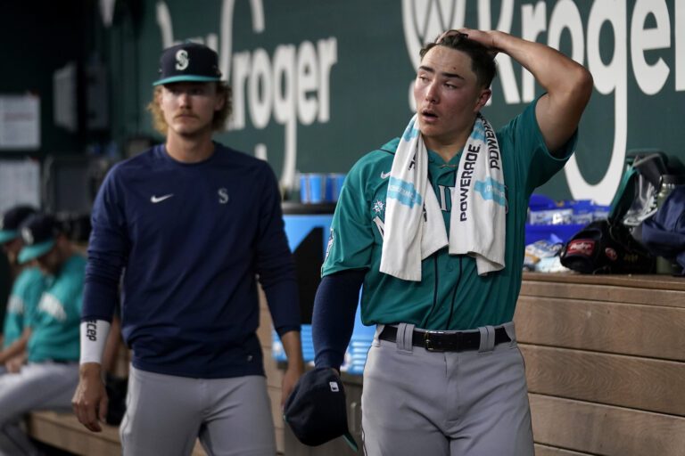 Seattle Mariners starting pitcher Bryan Woo, right, walks through the dugout as he talks with Bryce Miller, left.