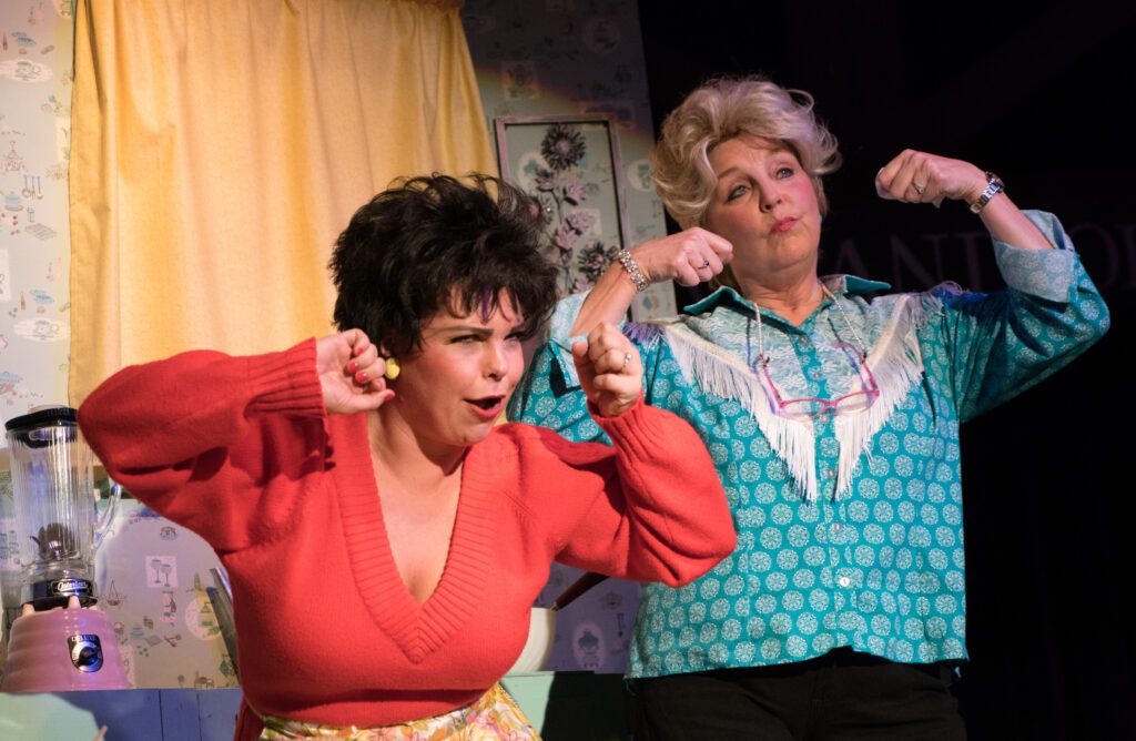 Ria Peth, left, and Kelly Visten reprise their roles as Patsy Cline and Louise Seger in “Always ... Patsy Cline,” as they make the crying motion with their hands on stage.