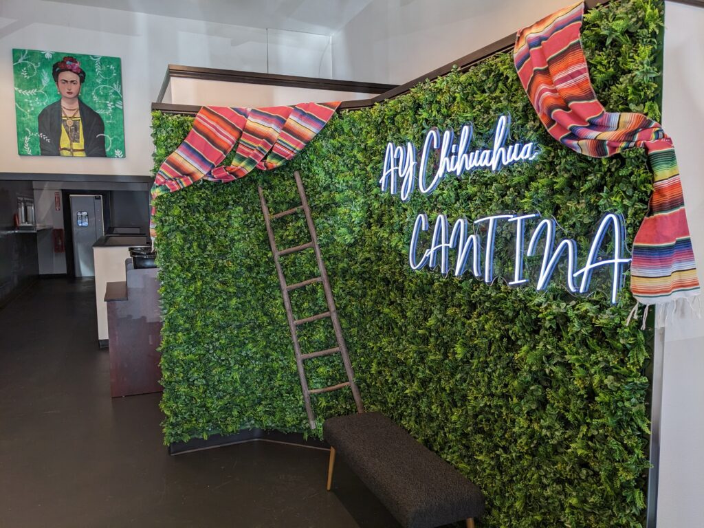 Entrance of Ay Chihuahua Cantina has a small space as a seating area that doubles as a photoshoot as it is decorated with a wall of plants.