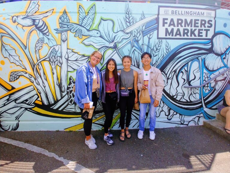 A group of people pose in front of the farmers market mural.