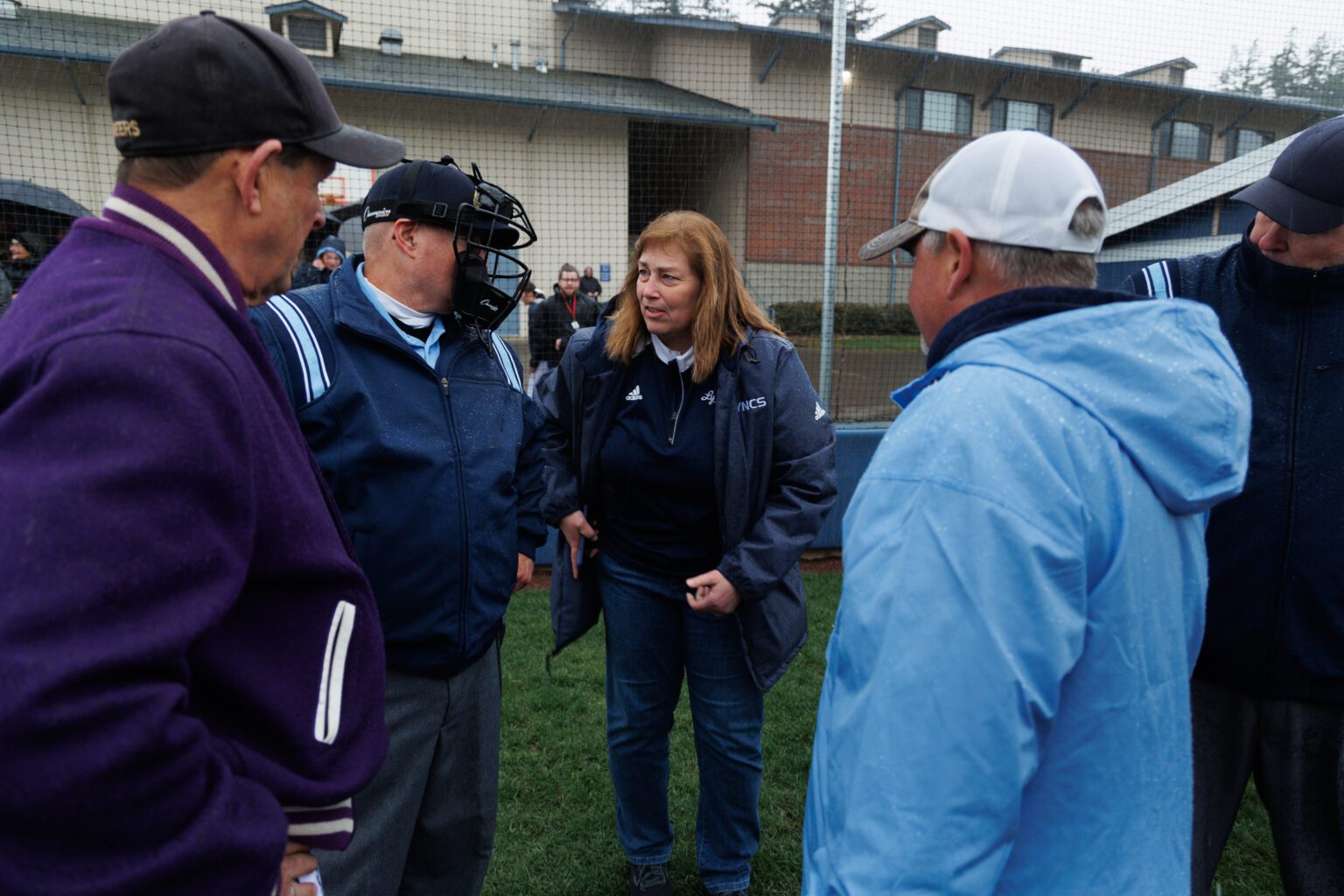 Lynden Christian Athletic Director Brenda Terpstra chats with umpires and coaches as others listen.