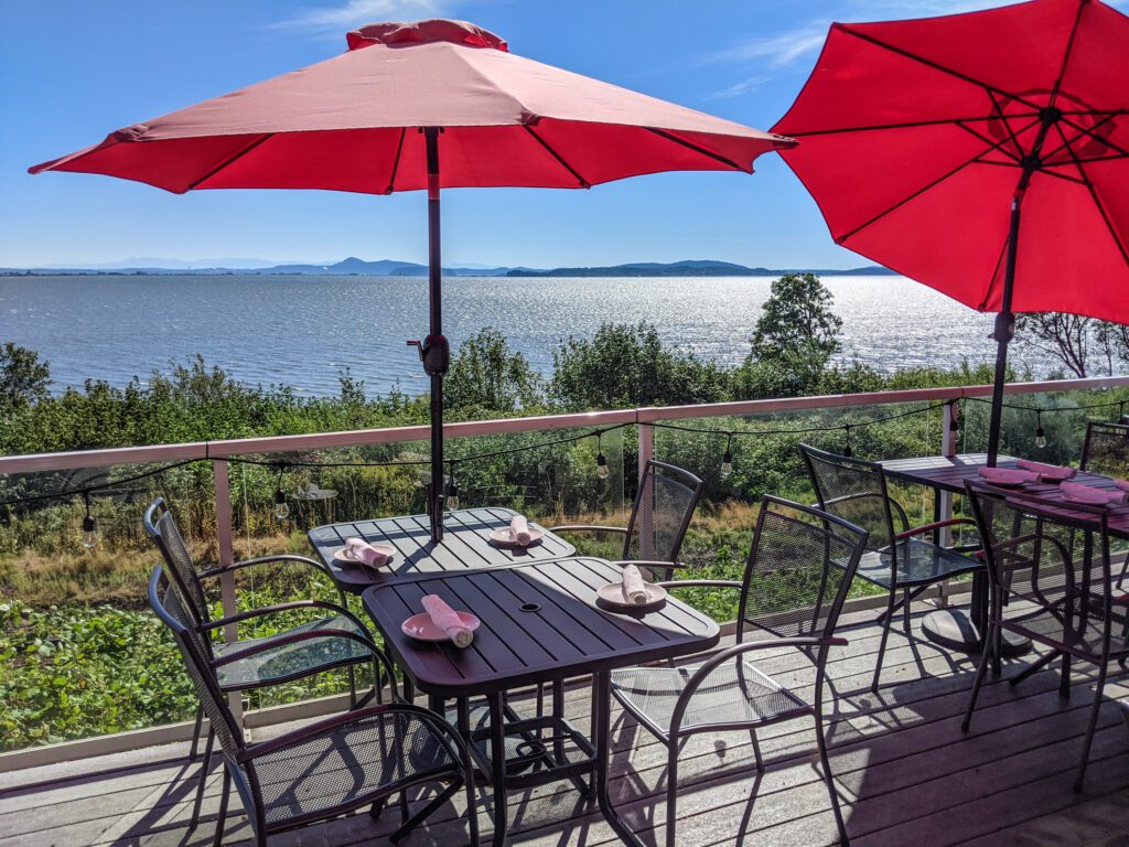 The outdoor seating of Chuckanut Manor has a deck with garden chairs, tables and bright red umbrellas.