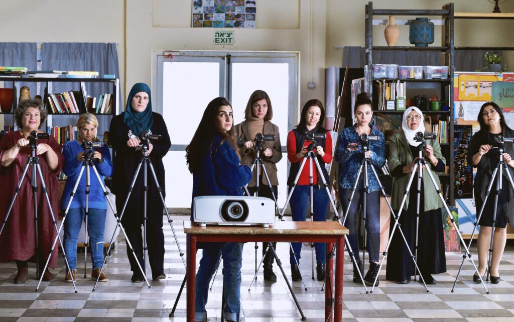 A group of Arab and Jewish women take a group photo with each of them with a camera on a tripod in front of them.