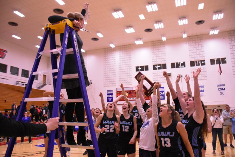 Veteran WWU women's basketball Coach Carmen Dolfo, the Great Northwest Athletic Conference coach of the year, hoists the net over her team.