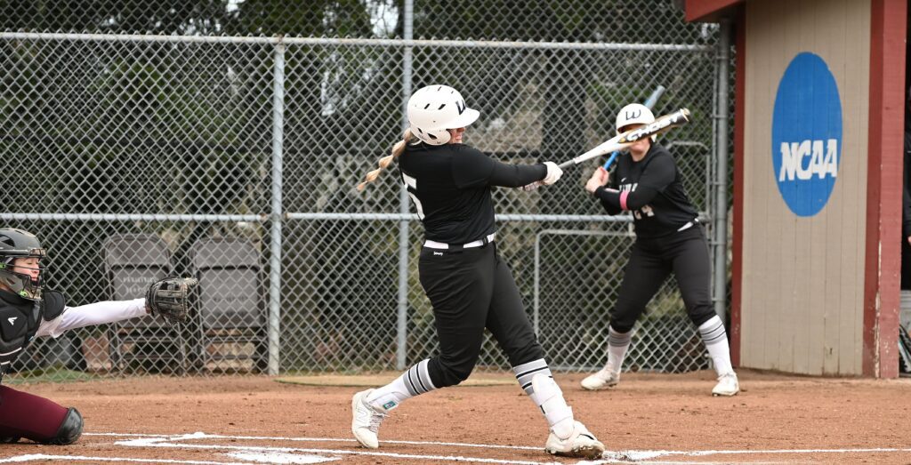 A batter swings with full force as a catcher waits behind them.