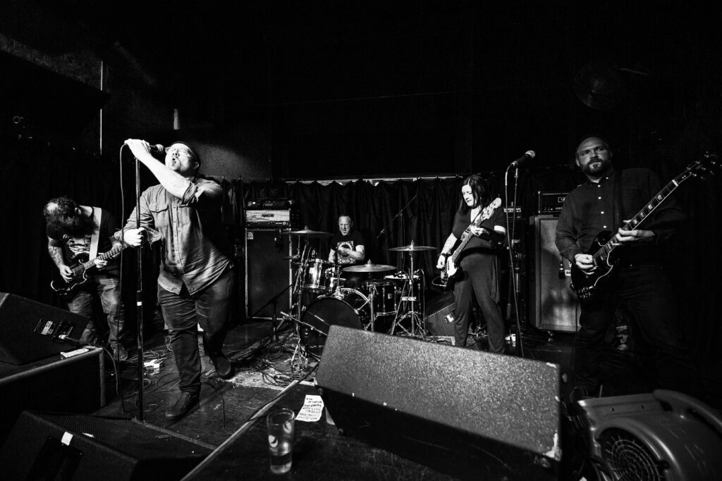 A black and white photo of the local metal favorites Dryland performing on stage.